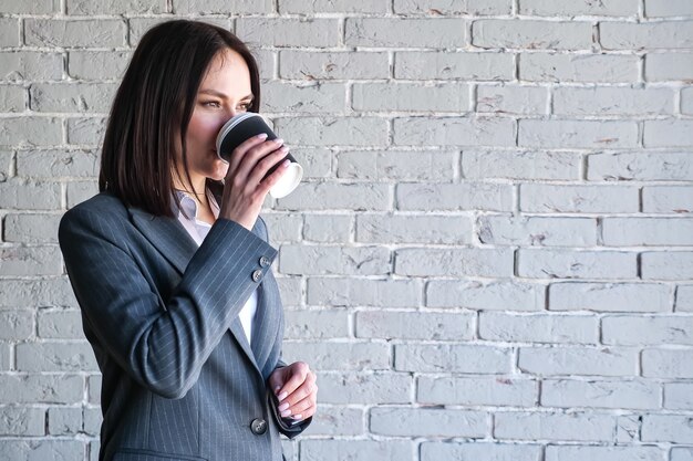 Smiling company manager in blouse and costume drinks coffee