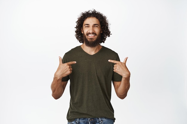 Smiling confident bearded man pointing fingers at himself with selfassured face expression selfpromoting standing over white background