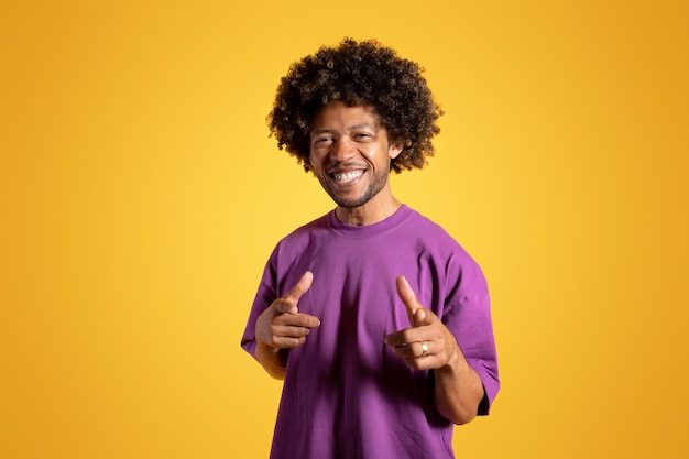 Smiling confident middle aged african american curly man in purple tshirt pointing fingers