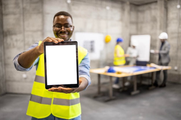 Smiling construction worker or engineer showing digital tablet display an building site