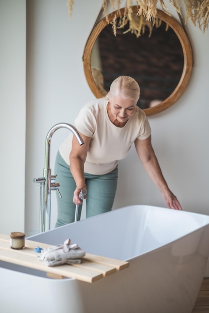 Foto femmina adulta contenta sorridente che si sporge sopra il bagno e che tiene il miscelatore del bicromato di potassio nella mano