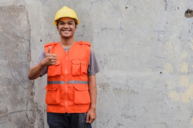 Smiling contractor man in helmet showing thumb up against wall background with copy space