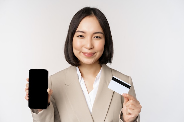 Smiling corporate woman in suit showing mobile phone screen and app on mobile phone smartphone screen standing over white background