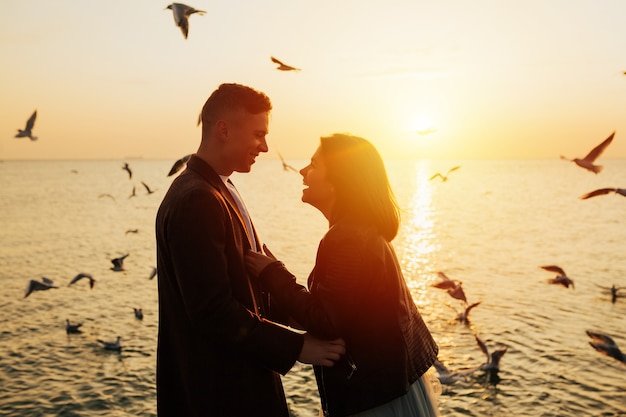 Smiling couple at beach enjoying view of the sea during sunset.