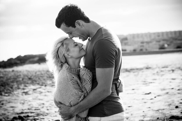 Photo smiling couple embracing at beach against sky