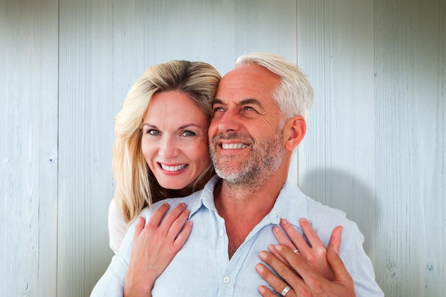 Smiling couple embracing with woman looking at camera against wooden planks