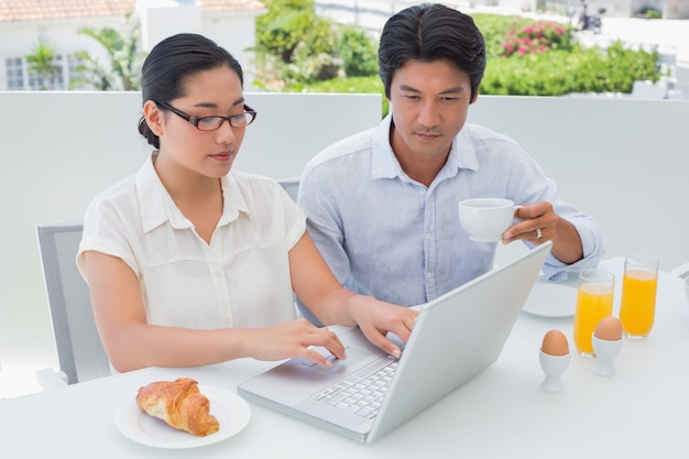 Smiling couple having breakfast together using laptop