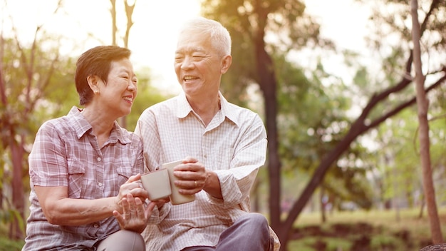 Photo smiling couple having drink while sitting in park