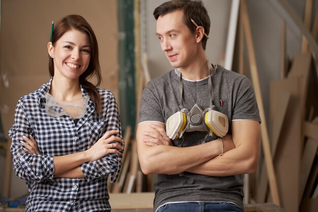 Smiling couple joiners with arms crossed looking at camera in workshop