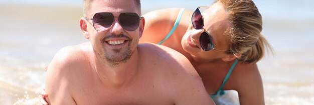 Smiling couple laying on coastline posing for memorable picture from vacation