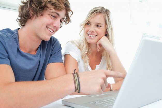 A smiling couple looking at the laptop with the woman looking at the man