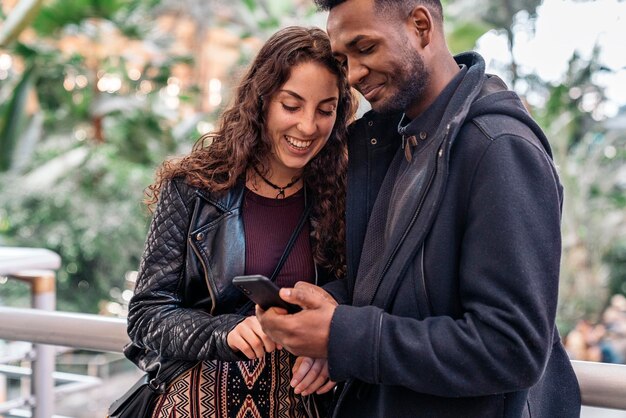 Photo smiling couple looking at phone while walking outdoors