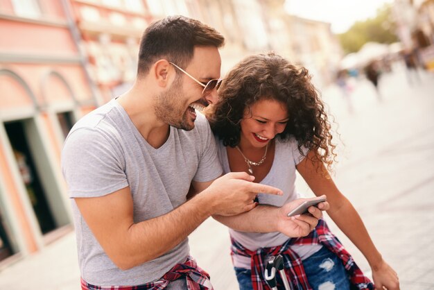 Smiling couple looking at photos on smart phone while standing on the street. Traveling concept.