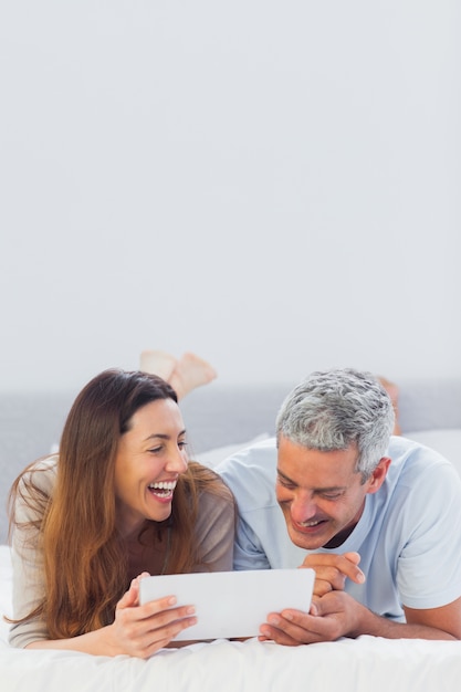 Smiling couple lying on bed using their tablet pc 