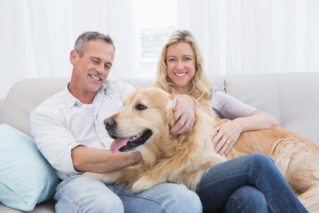 Smiling couple petting their golden retriever on the couch