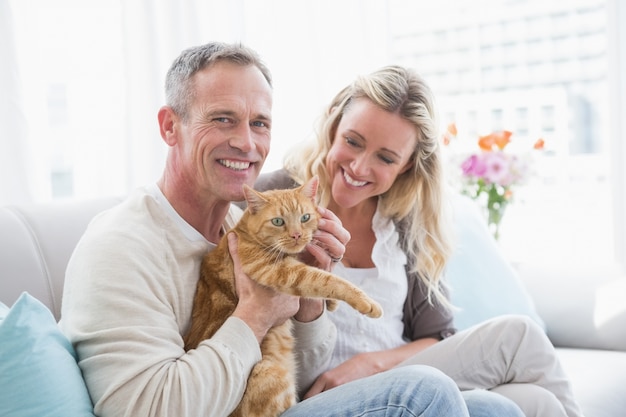 Smiling couple petting their gringer cat on the couch