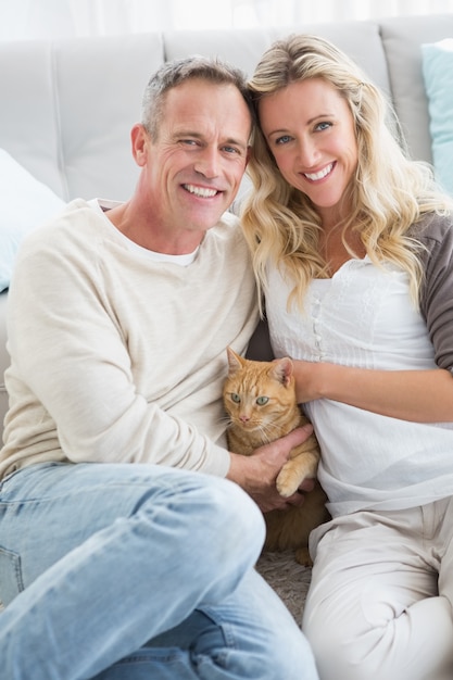 Smiling couple petting their gringer cat on rug