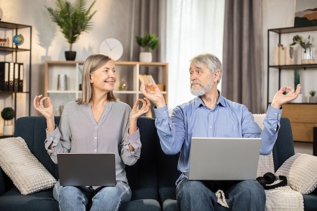 Smiling couple practicing yoga mudra on sofa in apartment