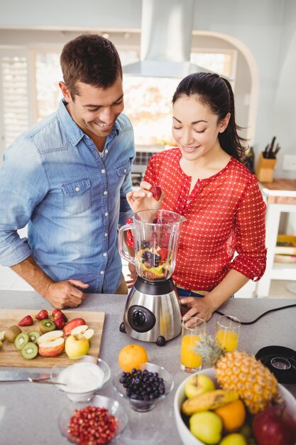 Smiling couple preparing fruit juice while standing at table