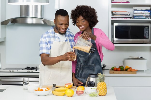 Smiling couple preparing fruit smoothie in kitchen