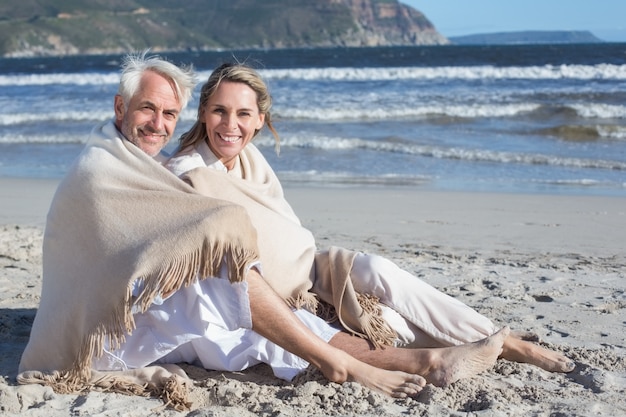 Smiling couple sitting on the beach under blanket