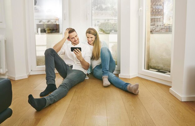 Smiling couple sitting on floor looking at cell phone