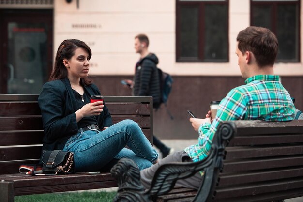 写真 コーヒーを飲みながらお互いに話しているベンチに座っている笑顔のカップル