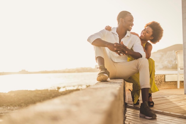 Smiling couple sitting on retaining wall against sky