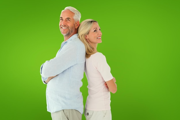 Smiling couple standing leaning backs together against green vignette