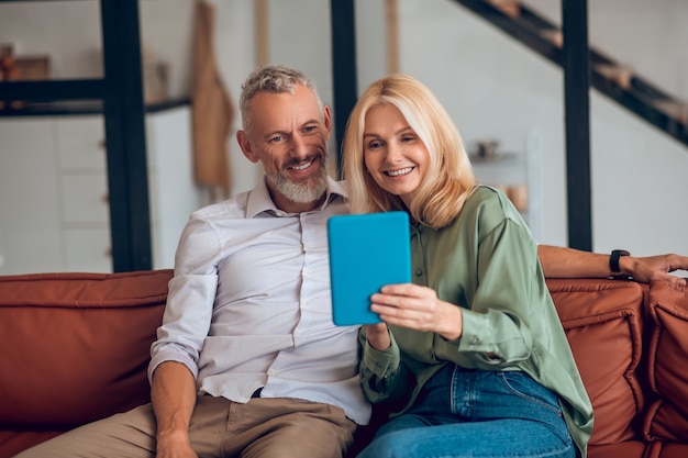 Smiling couple in sunglasses sitting on the sofa and having a video chat