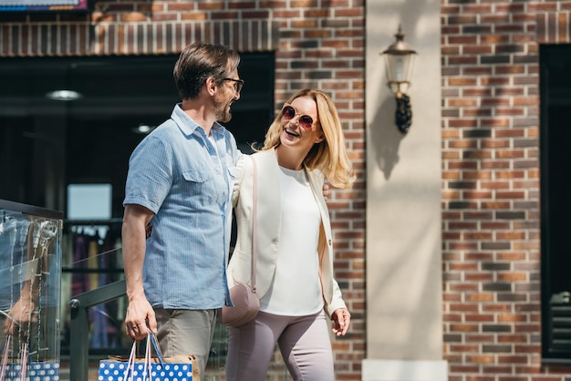 smiling couple in sunglasses walking with shopping bags