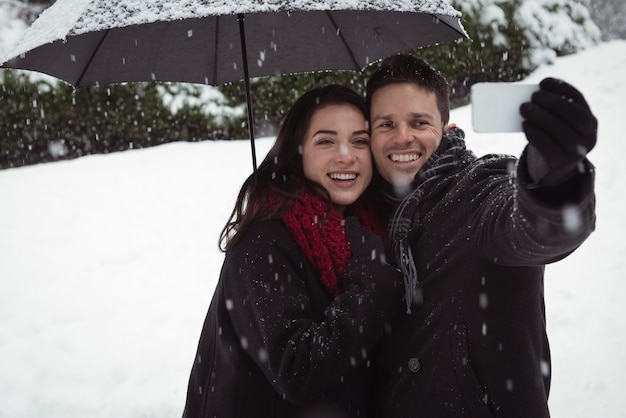 Smiling couple taking selfie on mobile phone during snowfall