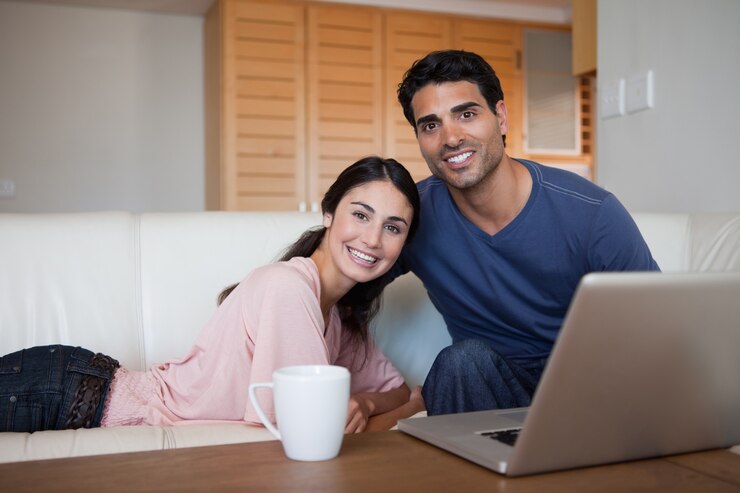 Photo smiling couple using a laptop while having a tea