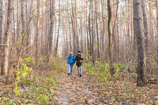 秋の自然な背景の上にバックパックを持って歩く笑顔のカップル。