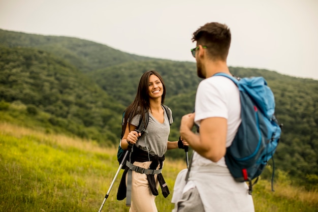 Smiling couple walking with backpacks over green hills