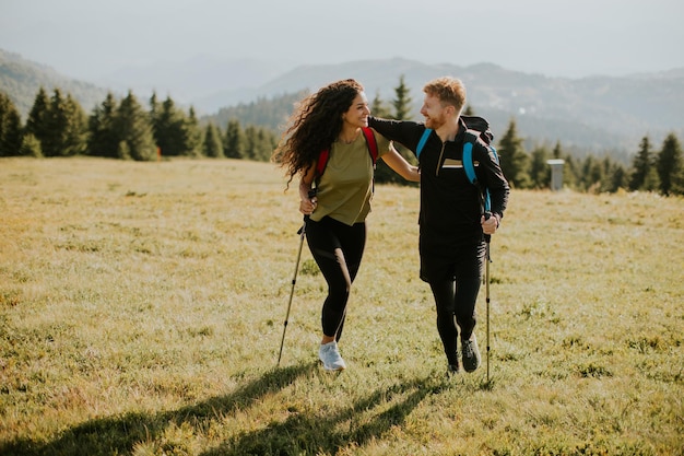 Smiling couple walking with backpacks over green hills