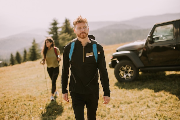 Smiling couple walking with backpacks over green hills