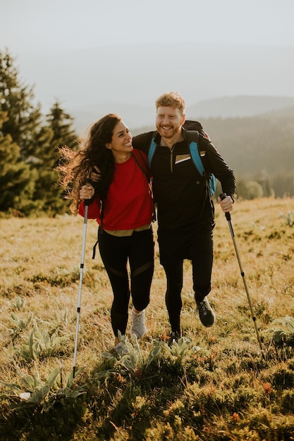 Smiling couple walking with backpacks over green hills