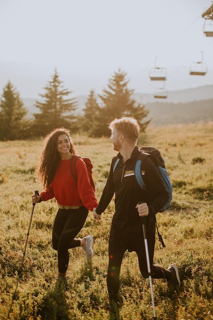 Smiling couple walking with backpacks over green hills