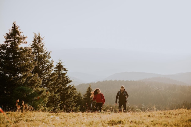 Smiling couple walking with backpacks over green hills