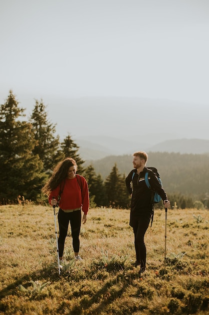 Smiling couple walking with backpacks over green hills