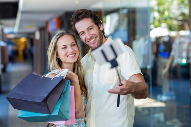 Smiling couple with shopping bags taking selfies with selfiestick