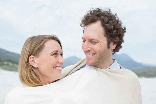 Smiling couple wrapped in blanket at beach