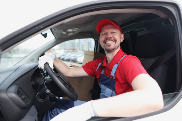 笑顔の宅配便の運転手が車のホイールの後ろに座っています