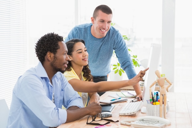 Smiling coworkers using computer together and pointing the screen