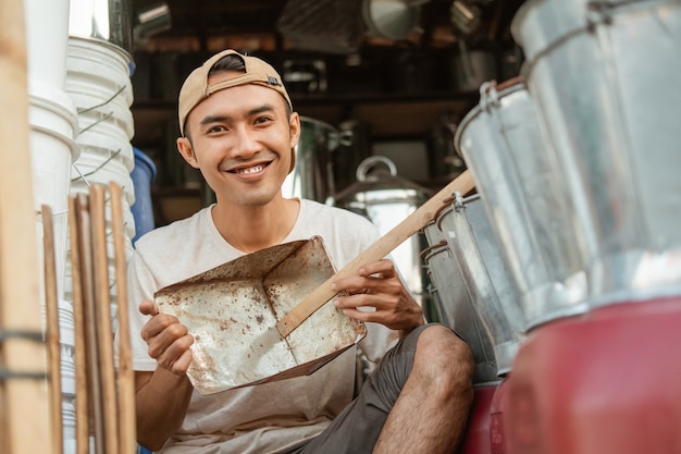 Foto sorridente artigiano in possesso di una paletta per la spazzatura quando mostra davanti al negozio di elettrodomestici