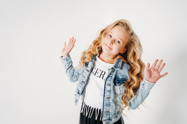 Smiling curly hair tween girl in denim jacket and black tutu skirt with raised hands on white  isolated