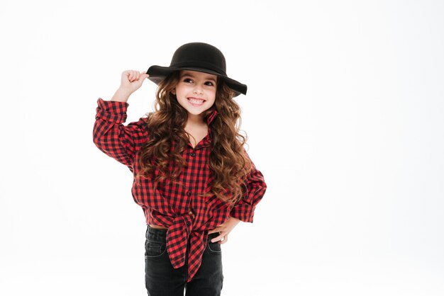 Улыбающаяся кудрявая маленькая девочка в клетчатой рубашке и шляпе