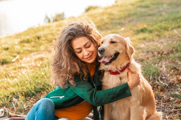 彼女のペットのゴールデンレトリーバー犬を抱いて笑顔の巻き毛の女性