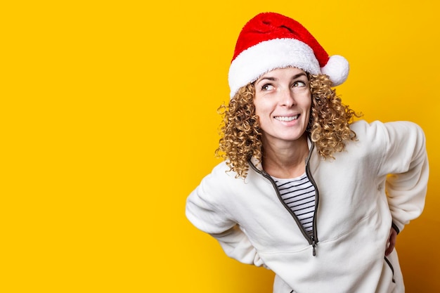 Smiling curly young woman in a santa hat on a yellow background